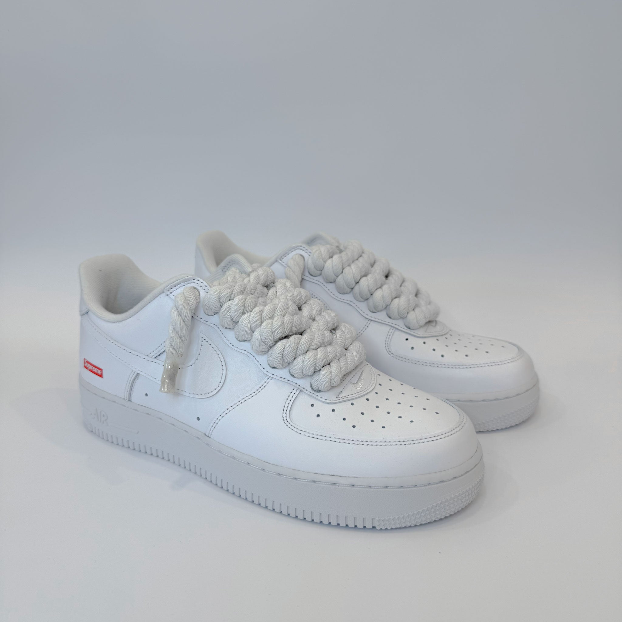 Pár custom Nike Air Force 1 Low Supreme White – minimalistické biele tenisky s prémiovými bielymi rope šnúrkami.