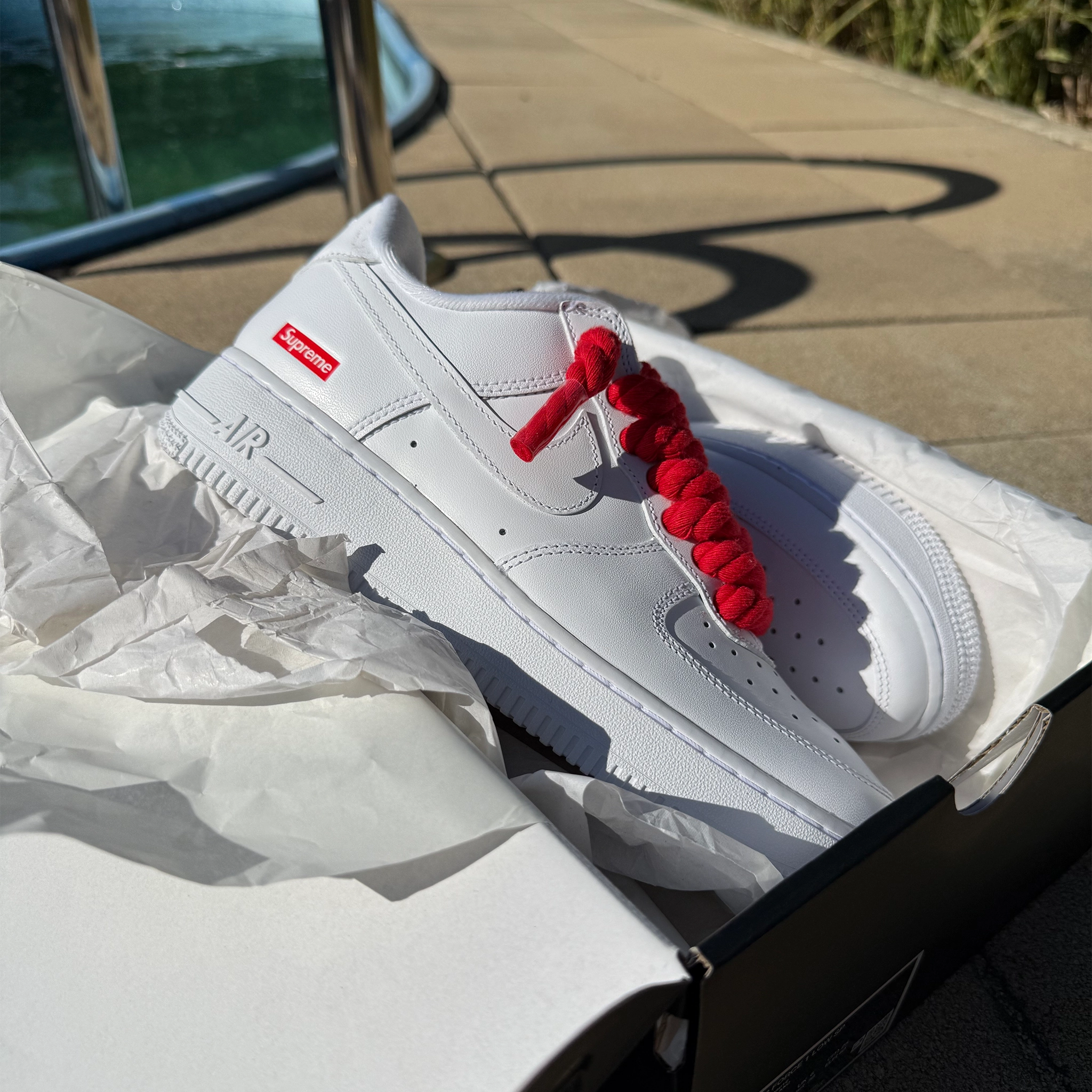 Pár custom Nike Air Force 1 Low Supreme White – ručne upravené biele tenisky s výraznými červenými rope šnúrkami.